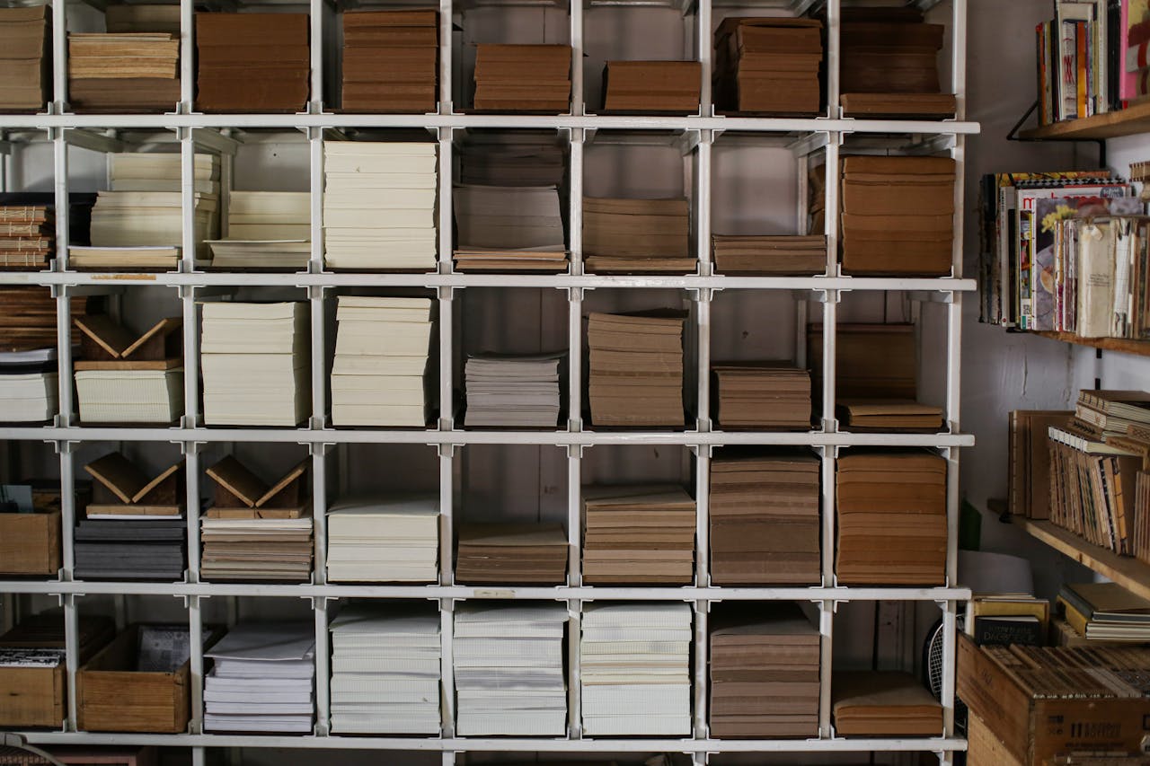 Neat stacks of various books and papers arranged on white shelving units.