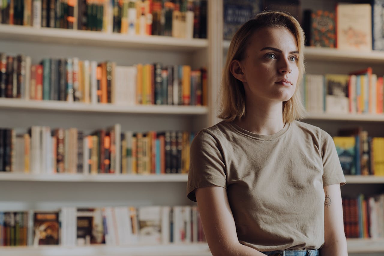 A young woman stands in a bookstore surrounded by colorful bookshelves.